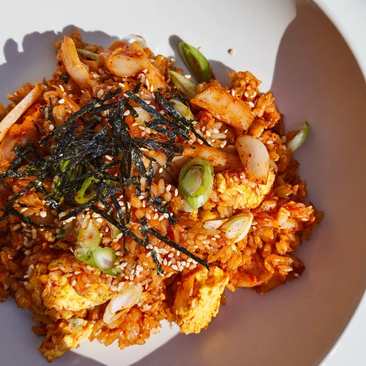 A close-up of vibrant spicy kimchi fried rice studded with colorful diced carrots, onions, and scrambled egg ribbons, garnished with fresh green onions and sesame seeds.  