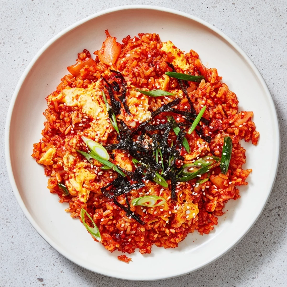 Served in a rustic ceramic bowl, the aromatic kimchi fried rice is topped with crispy roasted seaweed strips and a drizzle of sesame oil.