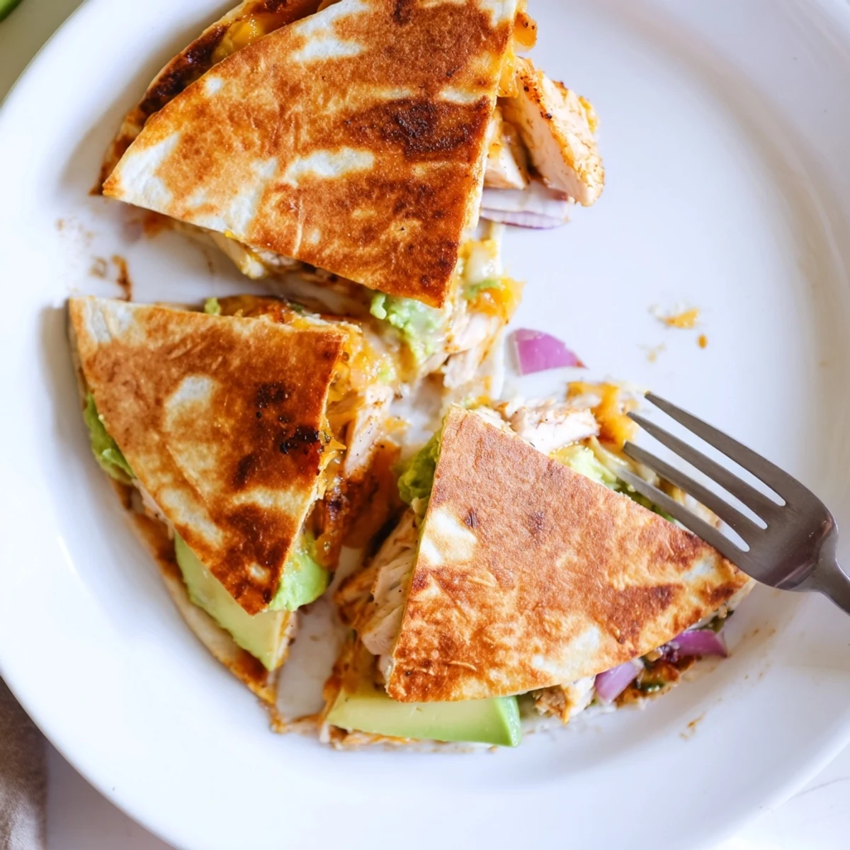 Golden-brown Chicken Avocado Quesadilla wedges showcasing melted cheese and creamy avocado mash, sliced on a rustic wooden board.
