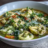A pot of Easy Tortellini Soup With Chicken Broth simmers on the stove, filled with tender pasta, carrots, and wilted spinach.
