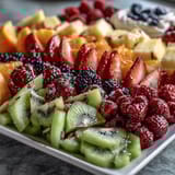 A colorful rainbow fruit table featuring strawberries, kiwi, blueberries, and oranges, served with fluffy coconut whipped cream.