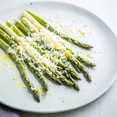 Close-up of freshly roasted asparagus with lemon, Parmesan, and parsley over a baking sheet.