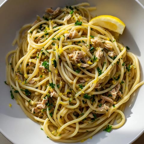 Savory lemon-garlic tuna spaghetti, a vibrant pasta dish served with lemon wedges and fresh herbs.