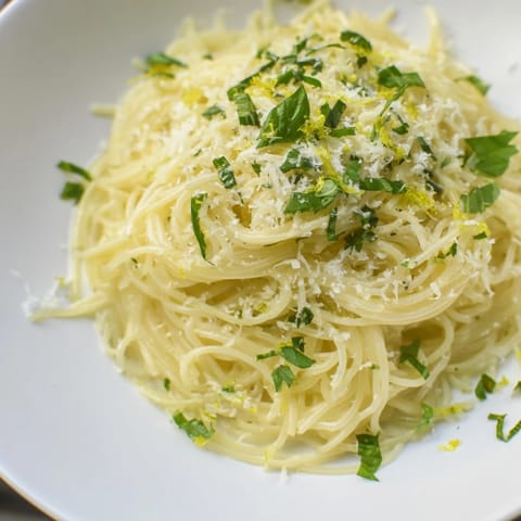 A close-up of steaming Lemon Capellini, showcasing the vibrant lemon sauce and fresh herbs.