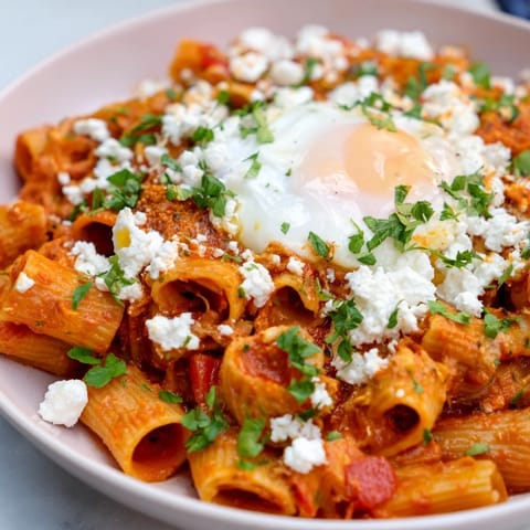 A close-up of Shakshuka Baked Pasta: piping hot pasta with perfectly poached eggs and fresh herbs.