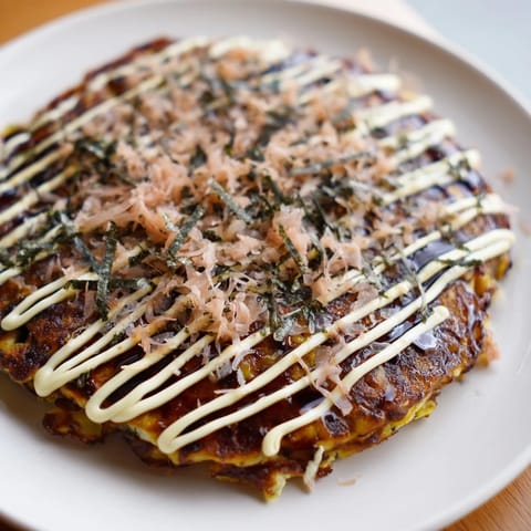 Golden-brown Japanese Okonomiyaki Pancakes topped with creamy mayo, tangy sauce, bonito flakes, and aonori.