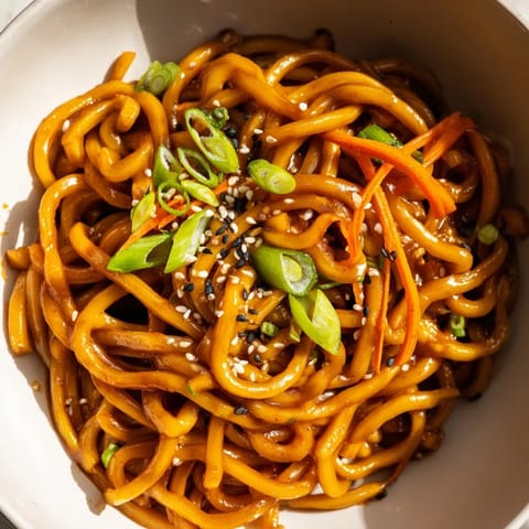 A fork lifts a portion of noodles coated in glossy garlic-butter sauce, with optional chili and bean sprouts visible.  