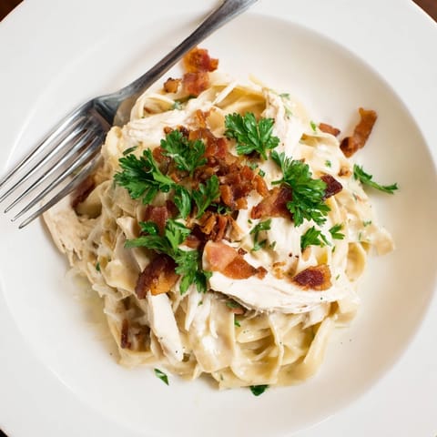 Steaming bowls of Chicken Carbonara feature al dente pasta coated in a velvety sauce with garlic and fresh parsley garnish.