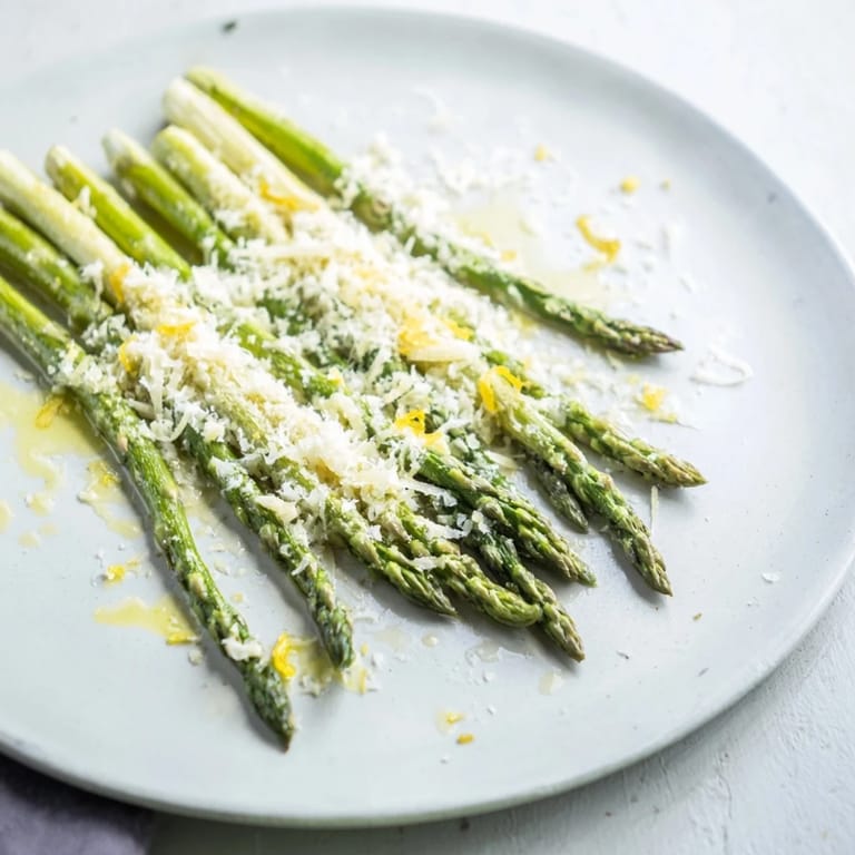 Close-up of freshly roasted asparagus with lemon, Parmesan, and parsley over a baking sheet.