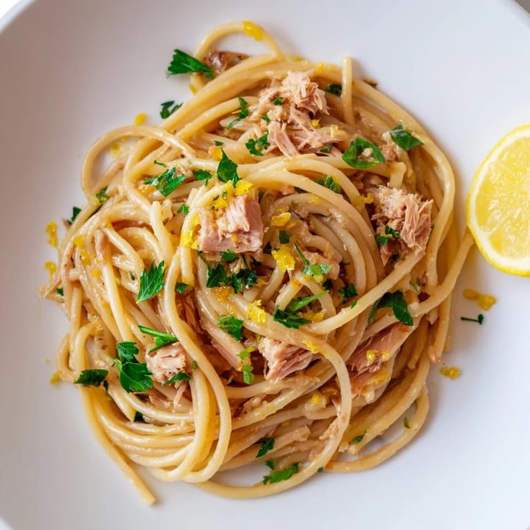 Tender spaghetti coated in a bright lemon-garlic sauce, topped with tuna for a flavorful meal.