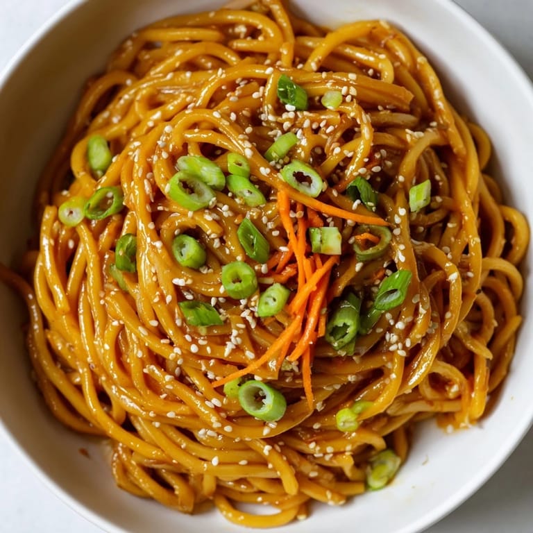 Close-up of a serving bowl featuring vibrant julienned carrots and toasted sesame seeds atop Asian Garlic Noodle Bowl.
